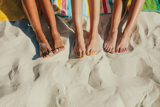 Group of female legs in sand with colorful pedicures