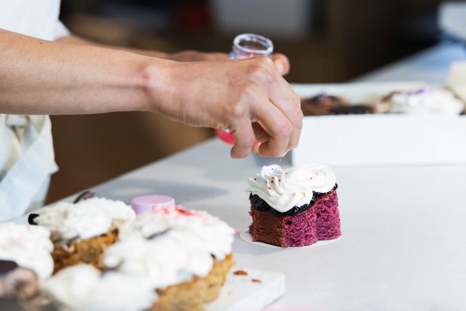 Crop baker decorating velvet cake with cream