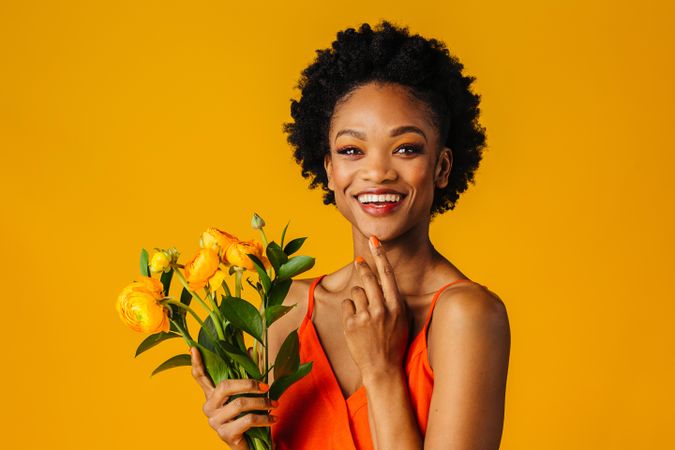 Happy Black woman holding a ranunculus bouquet with a finger to her chin