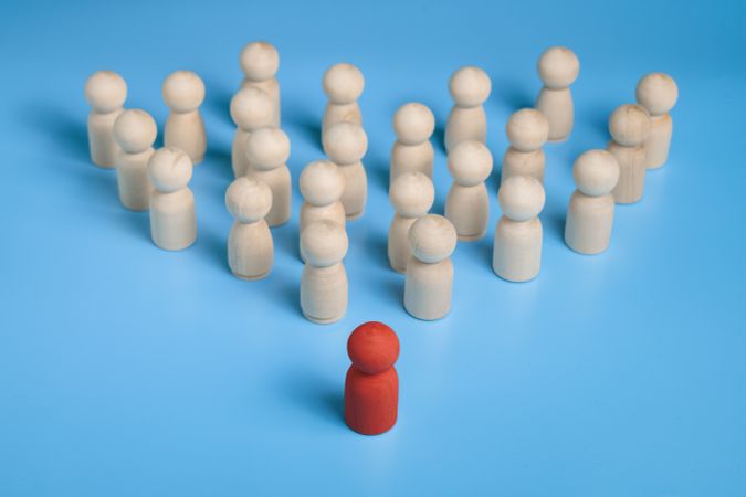 red wooden figure stand to the wooden group crowd. isolated on blue background. leadership and teamwork concept