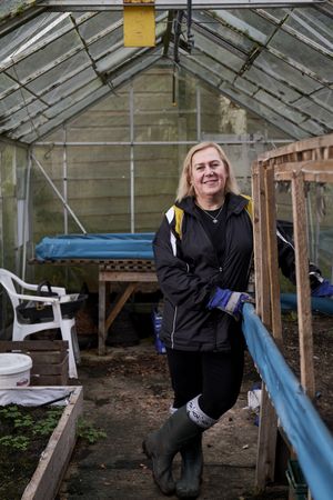 Woman with plant box inside greenhouse, vertical