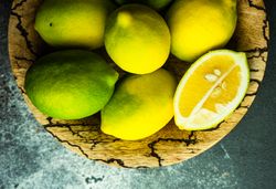 Top view of bowl of fresh lemons with one halved on top