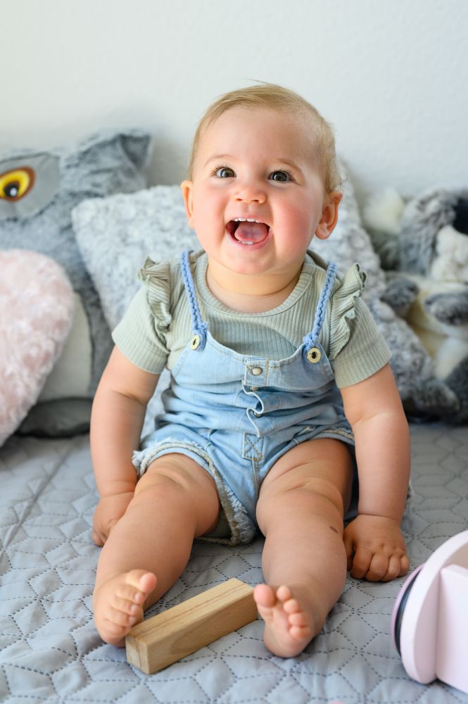 Cheerful baby sitting on bed looking at camera