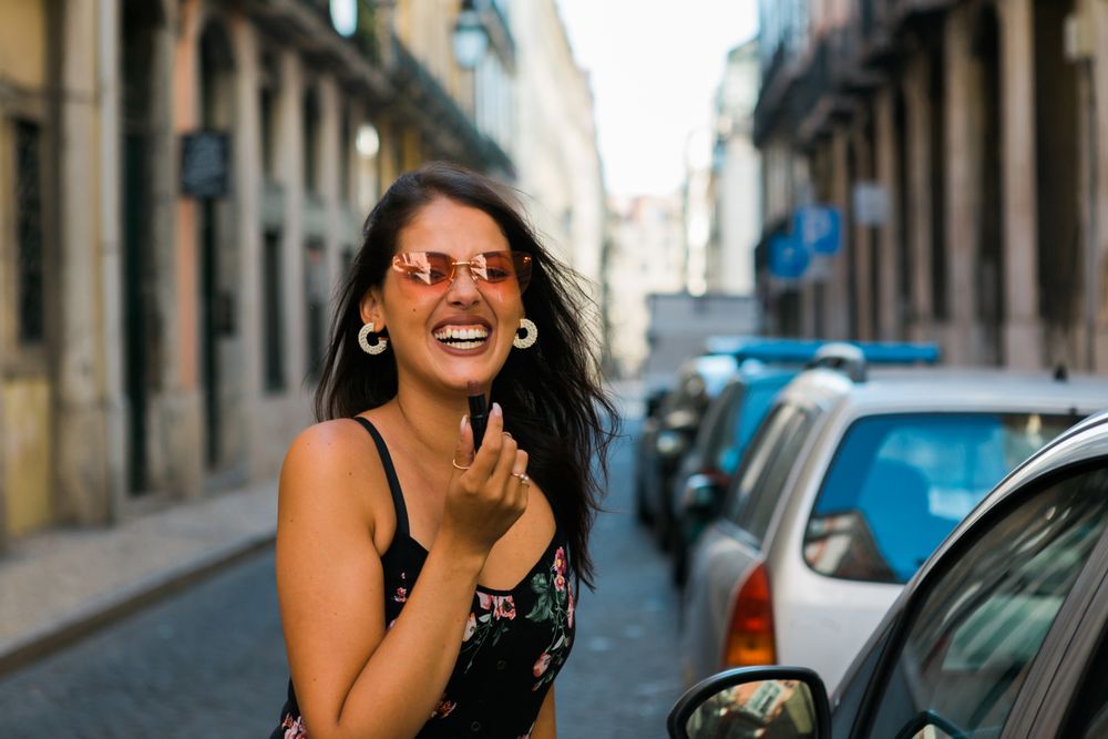 Confident woman in sunglasses applying lipstick on street