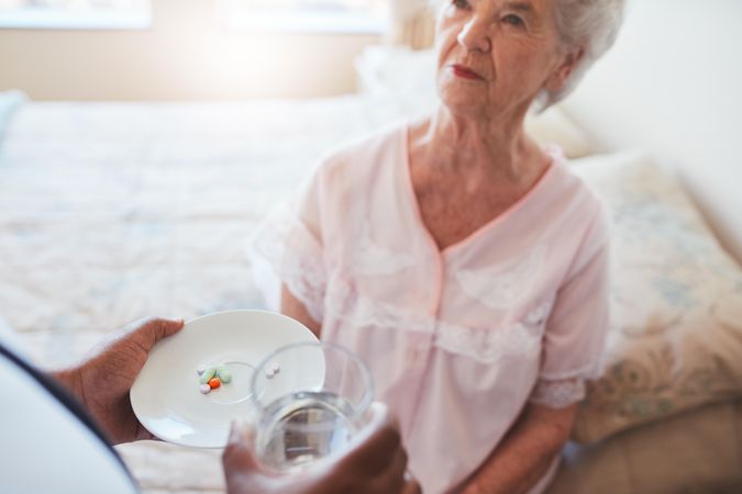Hand of nurse giving pills to elderly female patient
