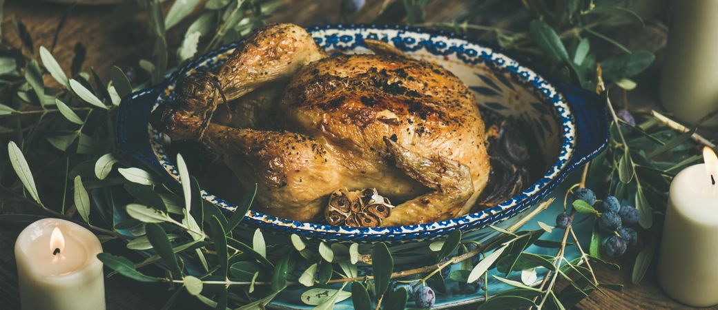 Centerpiece of roast chicken surrounded with decorative branches, and two candles