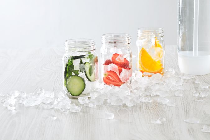 Three mason jars of infused water with distilled water bottle surrounded with ice