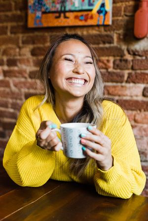 Portrait of woman holding a cup of coffee smiling at a coffee shop
