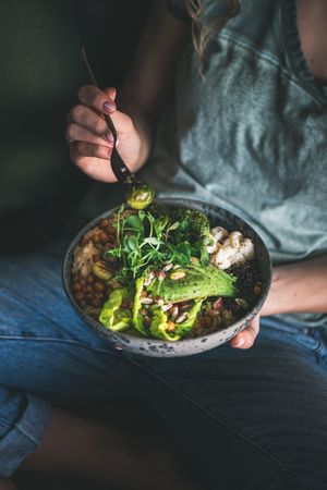 Woman in t-shirt and jeans sitting with fork in vegetarian bowl, vertical composition