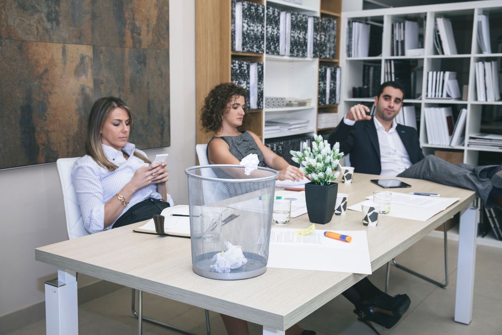 Colleagues bored in office and businessman throwing paper on basket