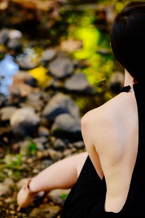 Back view of close up and  cropped view of woman’s shoulders sitting by a creek