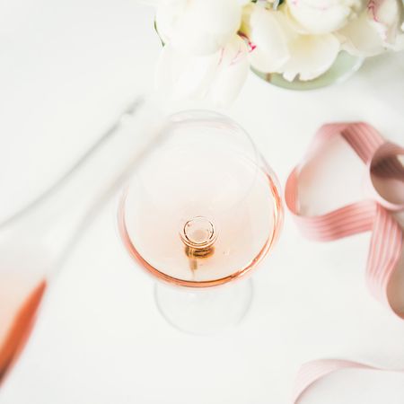 Glass of pink rose wine in the center with flowers and ribbon, square crop