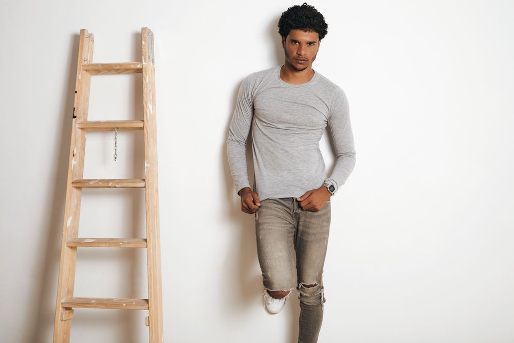 Man in grey leaning on wall next to ladder