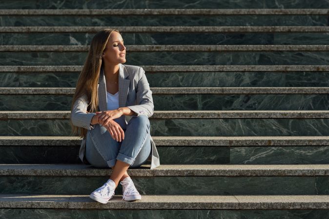Woman in blazer with eyes closed sitting on outside steps
