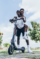 Black man riding on electric scooter in park with friend on back