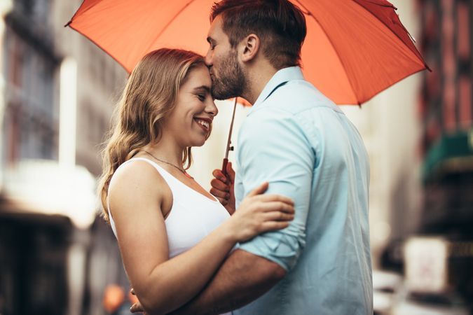 Romantic couple standing under an umbrella in street