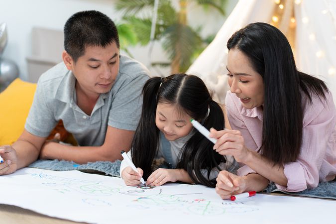 Happy Asian family drawing on paper together in the living room