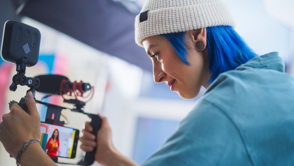 Young Female Cinematographer With Blue Hair Adjusts Camera Settings On Film Set, Capturing Vibrant, Dynamic Footage For A Modern Advertising Campaign Or Documentary.