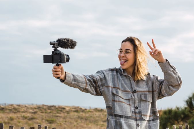 Happy female blogger showing tongue while shooting video on camera
