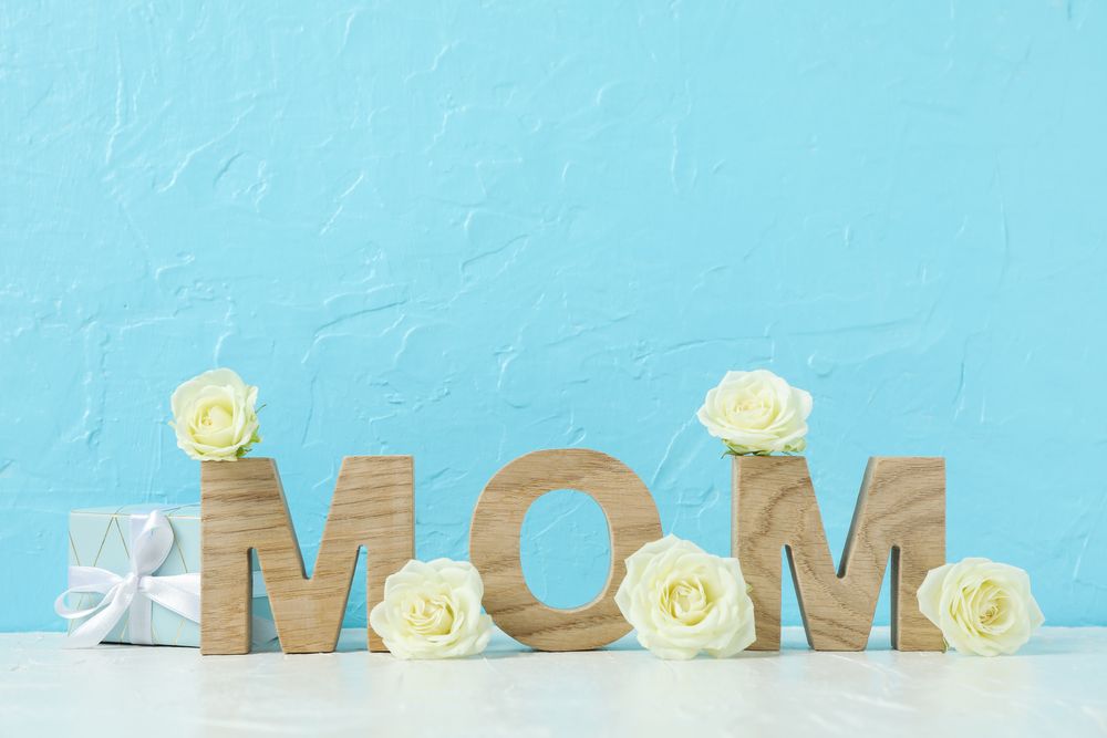 Inscription Mom with roses on pink table against color background, space for text