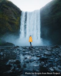 Person in yellow jacket standing near Skógafoss waterfall in Skógar, Iceland 4jAW85