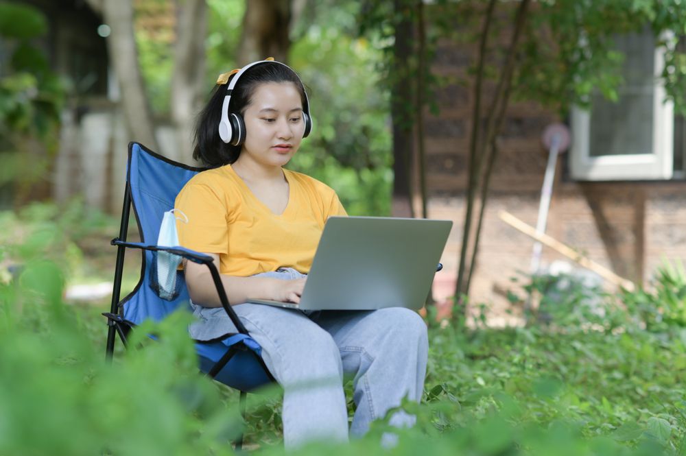 Young woman working on a laptop in the garden at home, work from home.