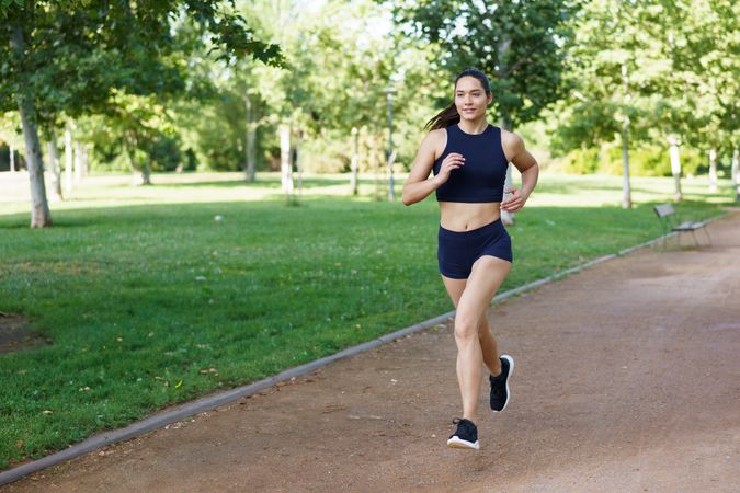 A determined young woman is jogging in the park on a bright, sunny day, focusing on her fitness and overall health