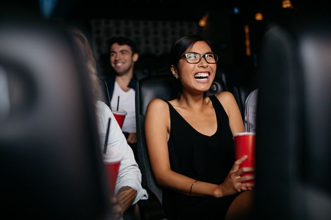 Young woman sitting in multiplex movie theater watching movie and laughing