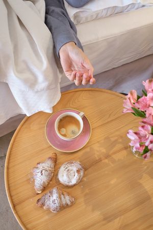 Crop female reaching out coffee cup in bedroom