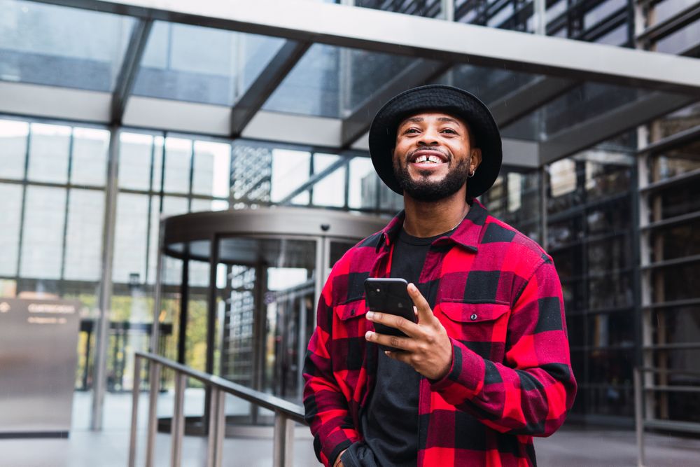Cheerful Black male with smartphone in contemporary building