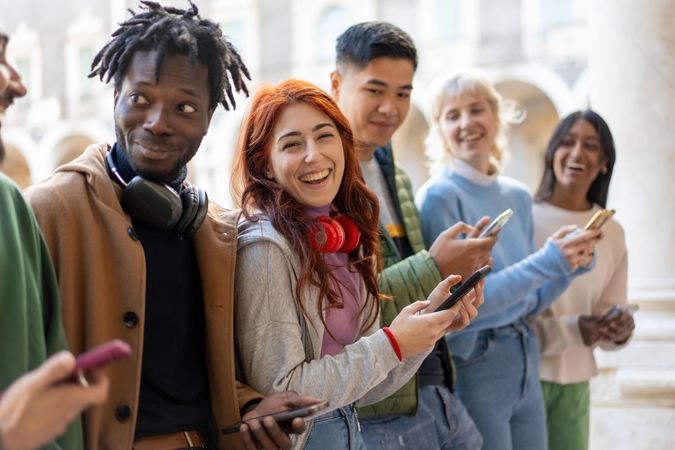 Happy multi-ethnic students standing around campus laughing and checking their phones