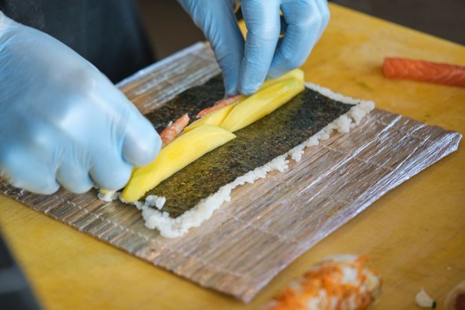 Unrecognizable chef making sushi with mango