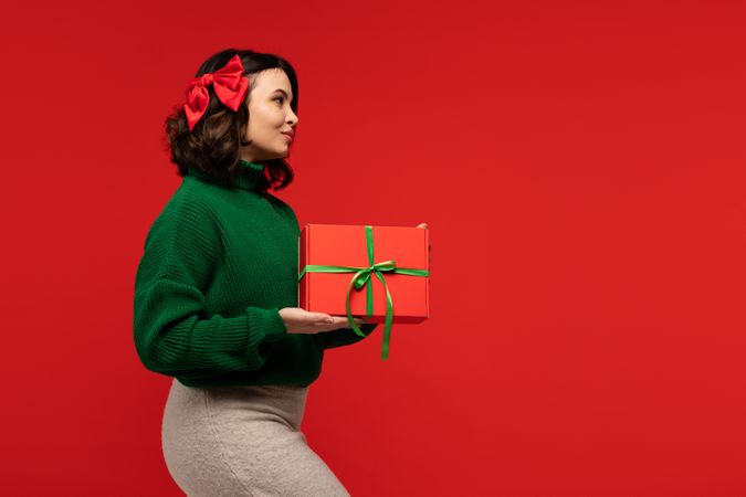 Woman in green sweater and bow, holding festive gift box