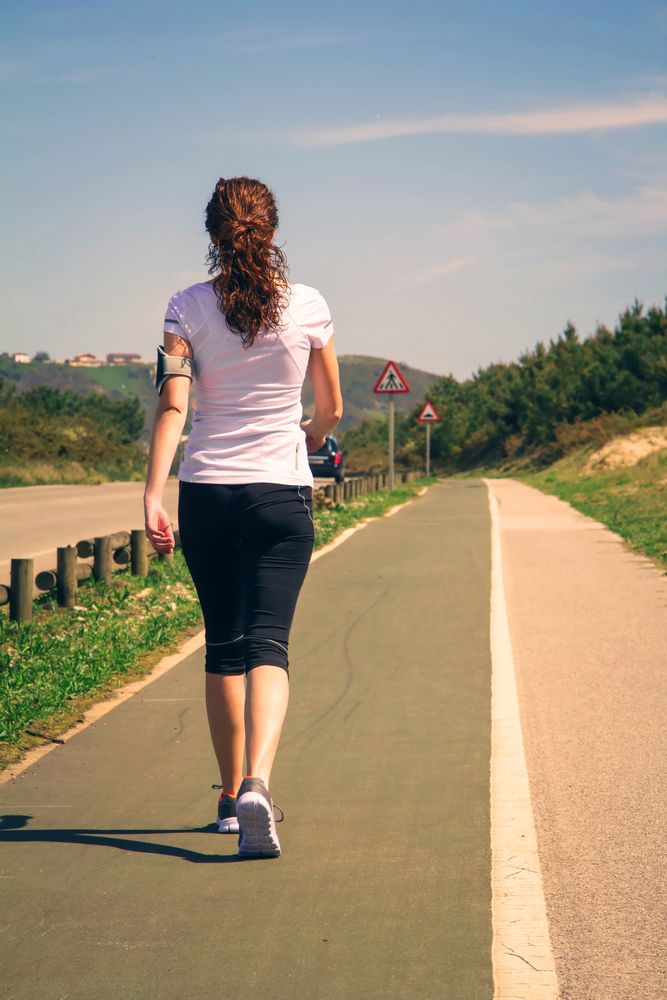 Back of woman in athletic gear strolling along road, vertical