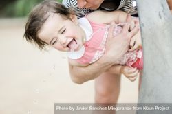 Little girl drinking water from fountain in her mother’s arms 4ZZOy4