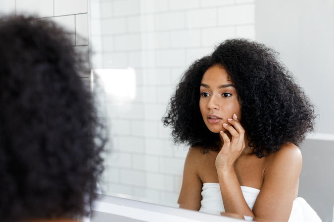 Curious Black woman observing herself in the mirror