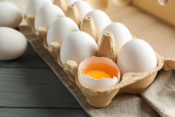 chicken eggs in carton box on wooden table, space for text and closeup