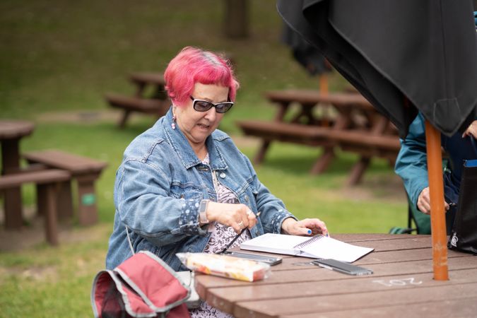 Older woman with pink hair drawing on park bench