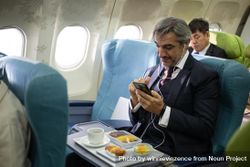 Man in suit on flight using smart phone while meal is served 48rBJ0