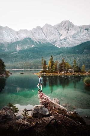 Man standing on rock beside lake and mountains