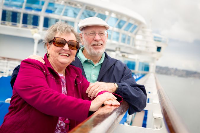 Smiling Mature Adult Couple Enjoying The View From Their Passenger Cruise Ship Railing.