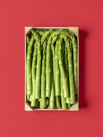 Green asparagus in a wooden box top view, isolated on a red background
