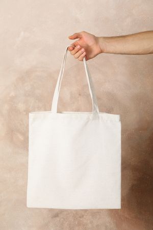 Male hand holding tote bag against brown background, empty space