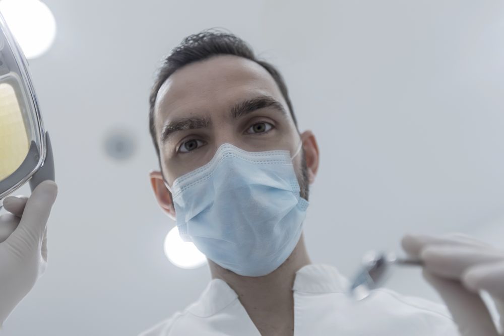 Low angle view of male dentist in medical mask holding dentist tools for dental procedure in clinic