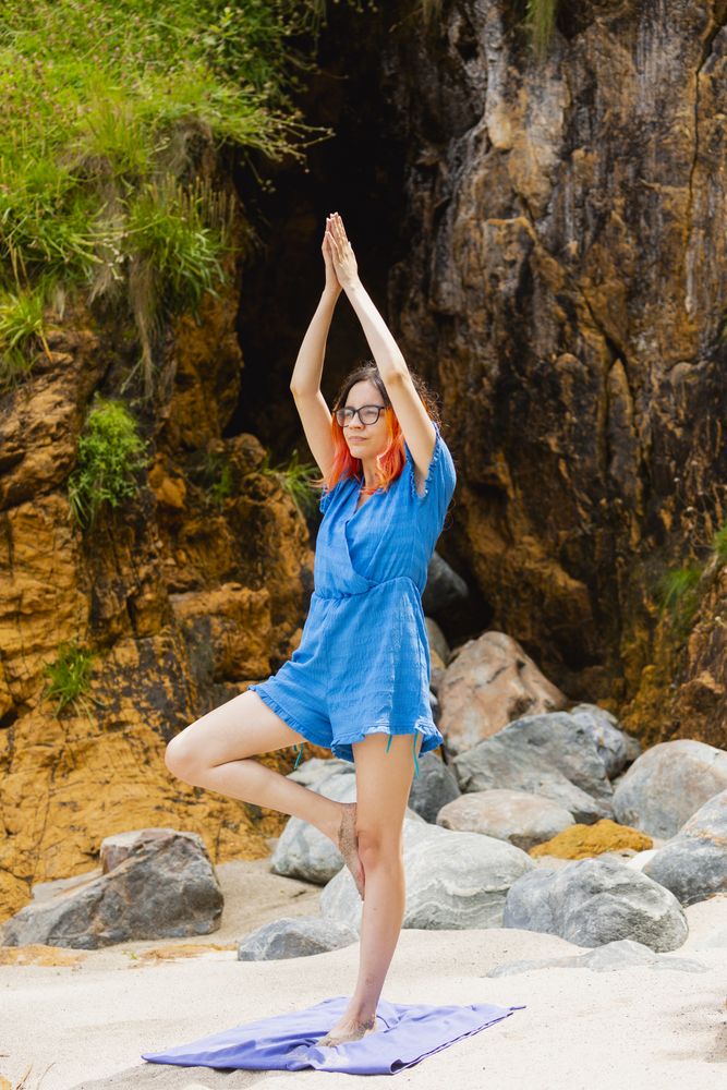 A young woman with orange hair practices yoga on a beach in summer