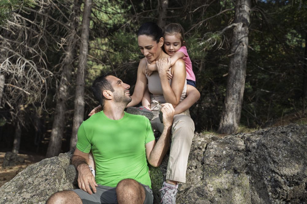 Happy family resting on rock during forest hike sharing loving moment