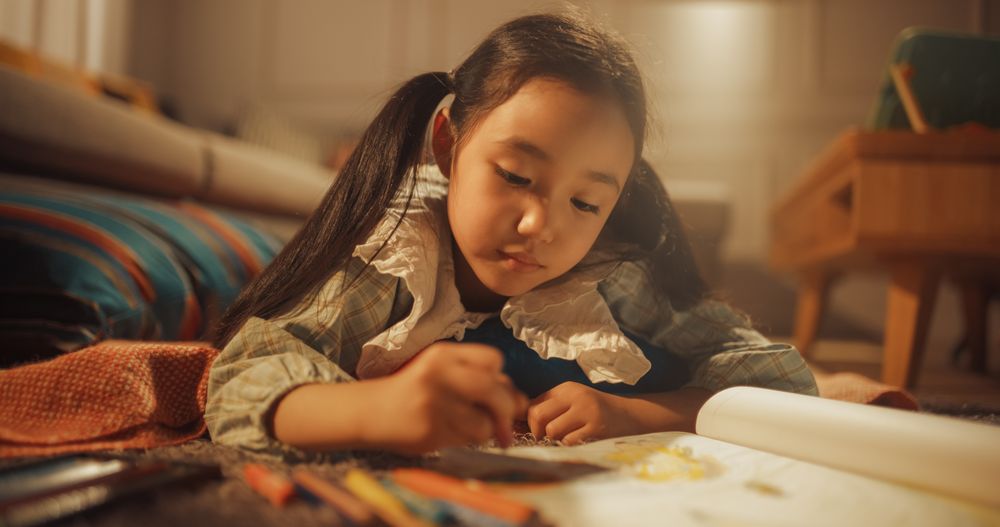 Evening Portrait of Cute Little Girl Drawing while Lying on the Floor in Living Room.