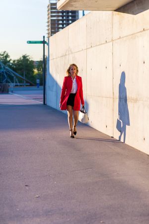 Front view of businesswoman wearing red jacket walking on the street with shadow