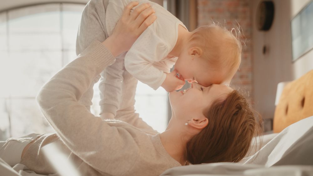 Young Caring Mother Playing and Nursing Adorable Baby at Home.