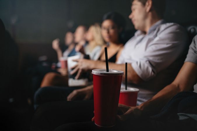 Focus on movie theater cup with friends behind